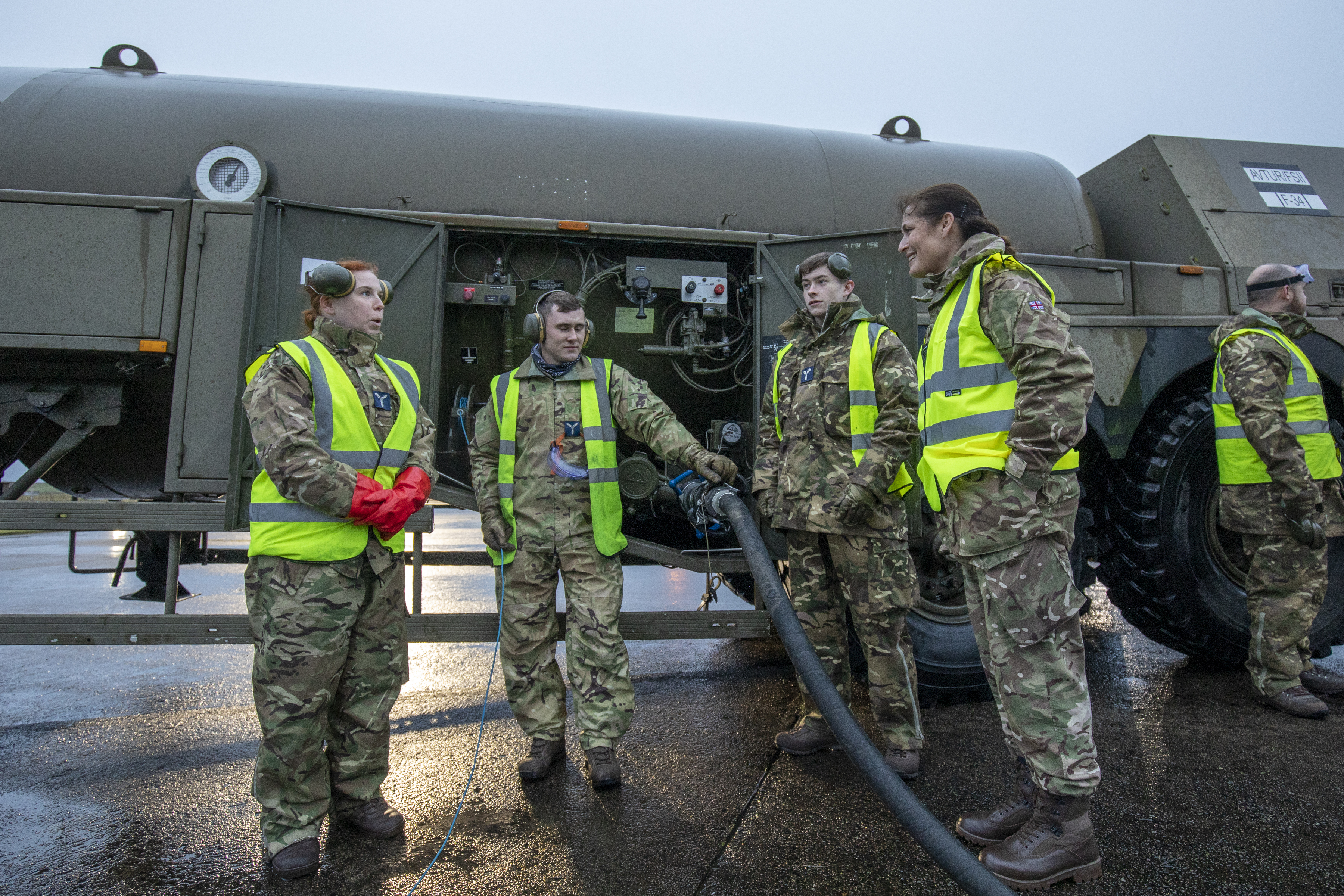 Personnel stand around refuelling tanker vehicle and pump.